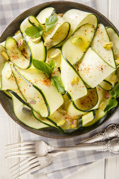Raw zucchini ribbon carpaccio with pistachios, chili pepper and mint close-up in a plate on the table. Vertical top view from above