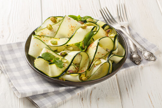 Zucchini Carpaccio is a raw courgettes salad with with pistachios, chili pepper and mint close-up in a plate on the table. Horizontal