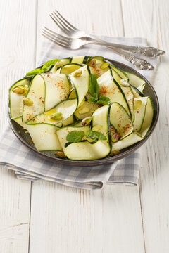 Delicious zucchini carpaccio topped with pistachios, chili pepper and mint close-up in a plate on the table. Vertical