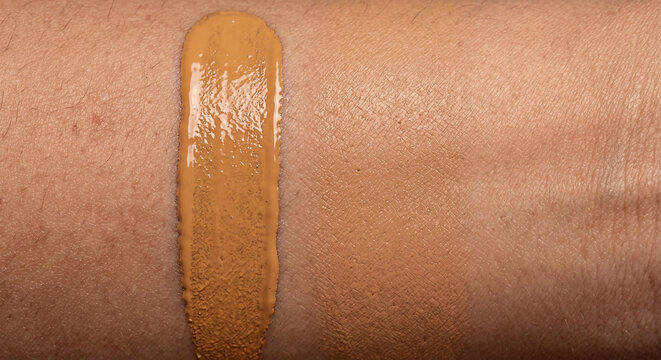 Close up view of a liquid foundation cream makeup swatch texture smeared onto a smooth human skin background. Cosmetic product color match testing concept.