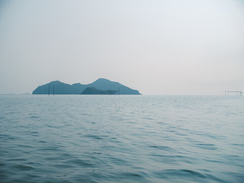 Serene ocean view of a distant green island against a hazy sky, calm natural background.