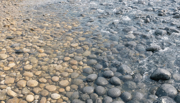 A shallow stream flowing over smooth, rounded river stones, with a clear contrast between wet, dark grey rocks and dry, light tan pebbles