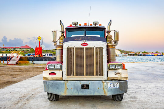 Willemstad, Curacao - May 25, 2026: Classic red Peterbilt semi truck with a heavy duty lowboy trailer parked at a concrete harbor terminal platform