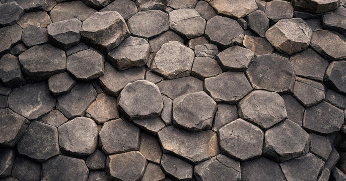 Close up view of dark gray basalt rock columns with natural hexagonal geometric patterns forming a solid stone surface texture background