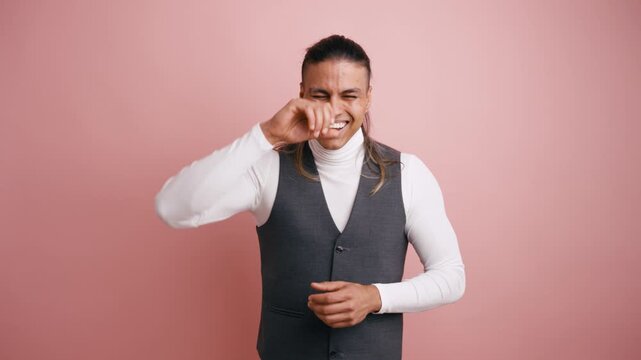 Amused latino guy laughing out loud and clapping his hands against a pink background. Charming man finding something hilarious