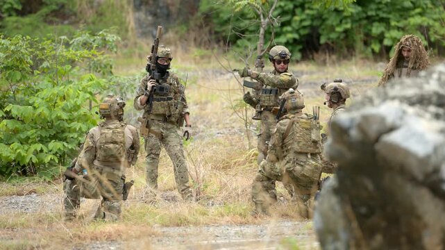 Military personnel conduct patrol and communication activities during a tactical field operation in a natural environment