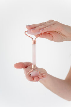 Hand holds rose quartz roller gently against white background
