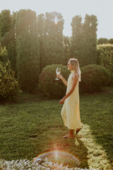 Woman in a yellow dress enjoys a drink while walking in a sunny garden © BGStock72