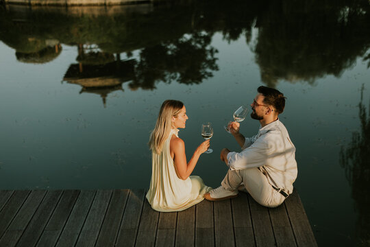 Couple enjoys drinks by the water at sunset near a dock