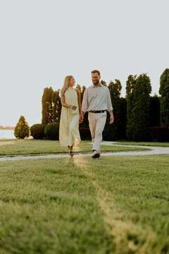 Couple walks together in park during sunset, holding hands in warm light