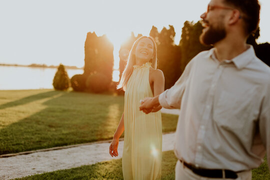 Couple walks hand in hand during sunset at a park near a lake on a warm evening