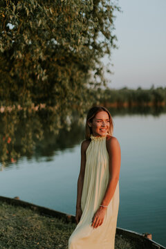 Young woman stands by water during sunset with trees in the background