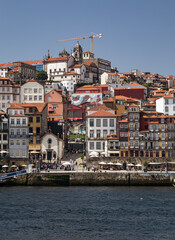 Fototapeta premium Vista panorámica vertical de la Ribeira de Oporto, Portugal, con sus coloridos edificios tradicionales sobre el río Duero, la iglesia de San Francisco y una grúa de construcción en un día soleado.