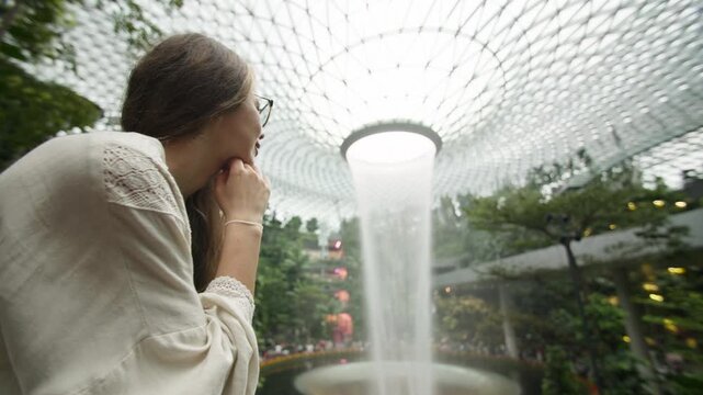 Female tourist admiring the indoor waterfall at Singapore airport surrounded by bionic architecture futuristic design tropical gardens and travel experiences in Asia