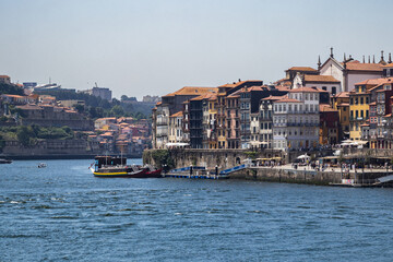 Obraz premium Vistas de la ribera de Oporto con sus edificios tradicionales de colores junto al rio Duero y barcos rabelos amarrados en el muelle en Portugal.