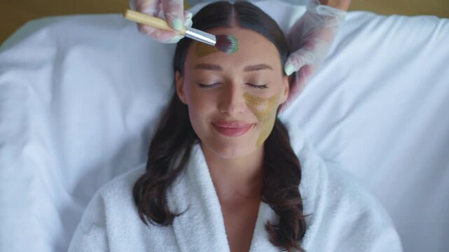 Woman receiving green clay mask application on face during spa treatment, 4K