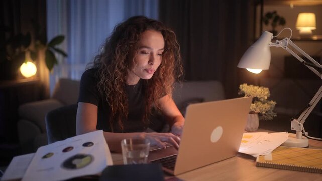 Young curly-haired woman having a sudden idea or eureka moment while working late on a laptop at night. Inspired female freelancer raising her finger at desk in a cozy home office