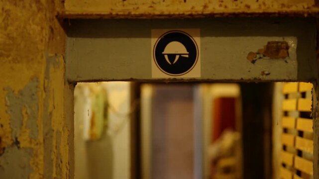 Signboard With Protective Helmet Icon At Entrance. Empty Old Abandoned Bomb Shelter. Ruins Cold War Underground Bunker 