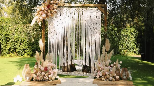 Wedding arch with macrame backdrop and floral arrangements in garden setting. 4K slow motion.