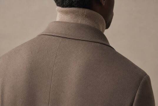 Professional man in tailored olive-brown suit jacket and cream turtleneck from behind, minimalist portrait with neutral background, modern business attire, corporate fashion concept