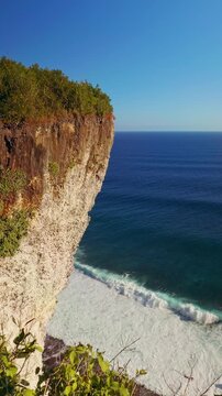Vertical video. Wide Angle View Of Karang Boma Cliff Rising Above Deep Blue Ocean And Powerful Waves, Coastal Adventure And Natural Wonder