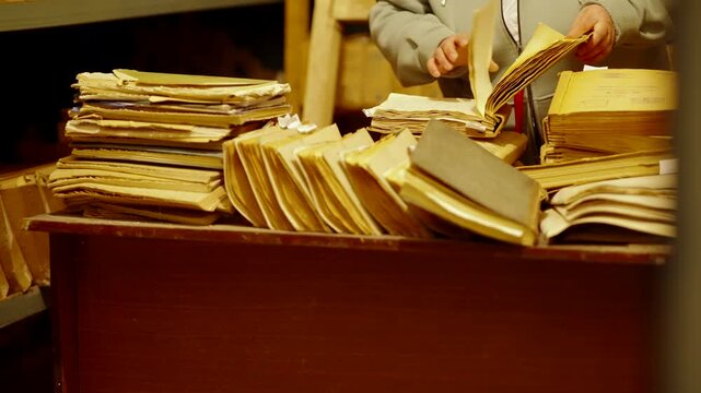 Person Searching Through Old Vintage Files. Archivist Flipping Pages Of Yellow Historic Folders. Repository Library 
