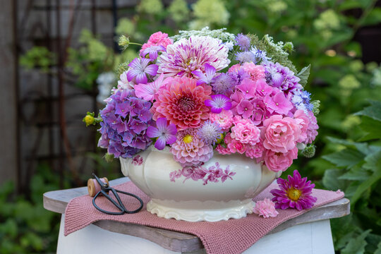 Blumen-Arrangement mit Dahlien, Rosen, Hortensienbl&uuml;ten, Federnelken, Wilder M&ouml;hre in vintage Suppenterrine im Sommergarten
