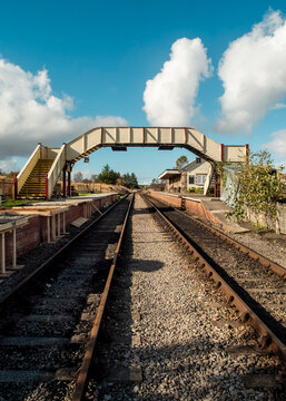 An empty heritage railway station with a traditional pedestrian footbridge spanning the tracks, reflecting a nostalgic and preserved setting for historic rail travel in the countryside.