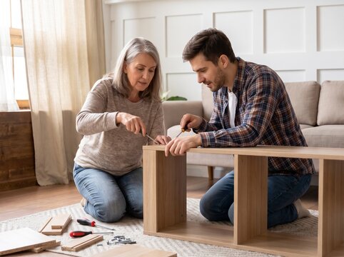 Senior mother and her adult son assembling flat pack wooden furniture together on the living room floor