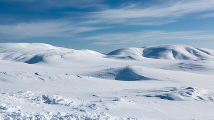 Fototapeta premium A vast snowy landscape of rolling hills and dunes under a clear blue sky with wispy clouds