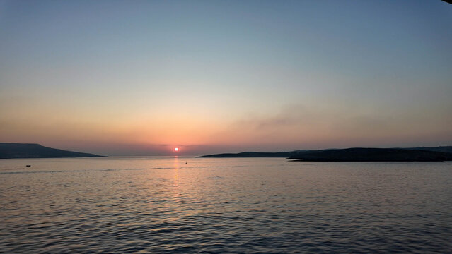 serene Sunrise over calm water in the evening sky with a tranquil fixed perspective from a distance, nature ambiance with blue and orange hues, clean background