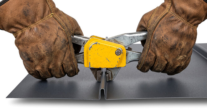 Hands in leather work gloves using specialized yellow metal seamer tool on standing seam roofing.