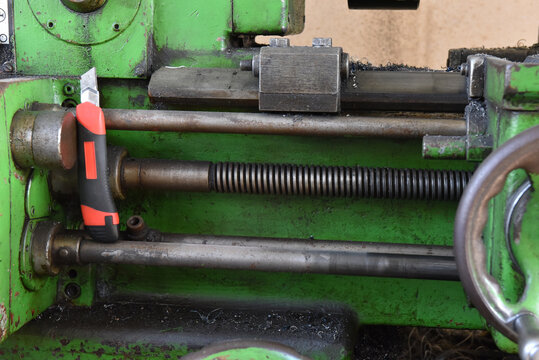 Industrial green metal lathe with utility knife in a workshop