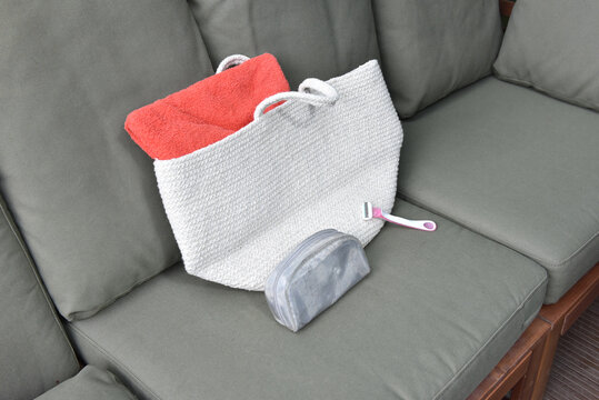 Woven tote bag with coral towel and grooming essentials on a grey outdoor sofa