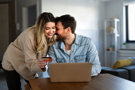 Smiling couple holding a credit card and shopping online at home with a laptop, online purchase
