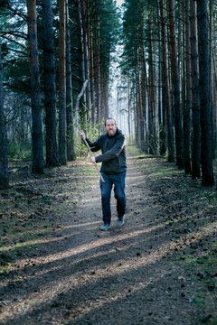 Intimidating Man with a Large Stick Walking Through a Pine Tunnel