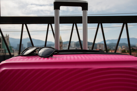 close view of black sunglasses on a pink rolling suitcase with batumi skyline behind, illustrating a ready for vacation mood, luggage details and contemporary city travel lifestyle