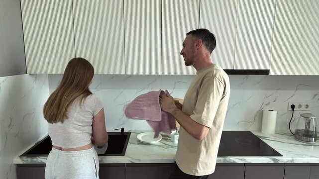 A young couple happily wash dishes in their modern kitchen