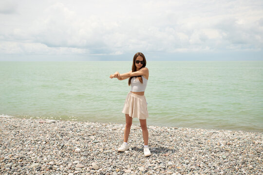 sporty teenage girl exercises on a pebble beach with the sea behind her, representing outdoor fitness, summer movement, healthy routine and active coastal lifestyle