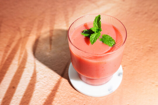 Vibrant pink strawberry protein smoothie in a glass over a shadowed background.