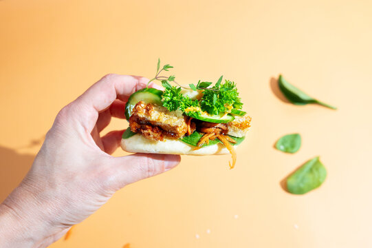 Close-up of a woman's hand holding a fluffy bao bun filled with tender chicken.