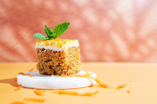 A slice of carrot cake served on a plate against a bright yellow background.