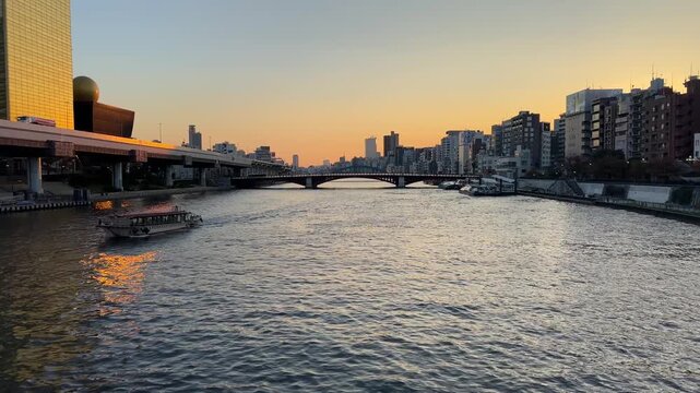 Tour boat navigating the Sumida River in Tokyo, Japan, with city skyline during golden hour