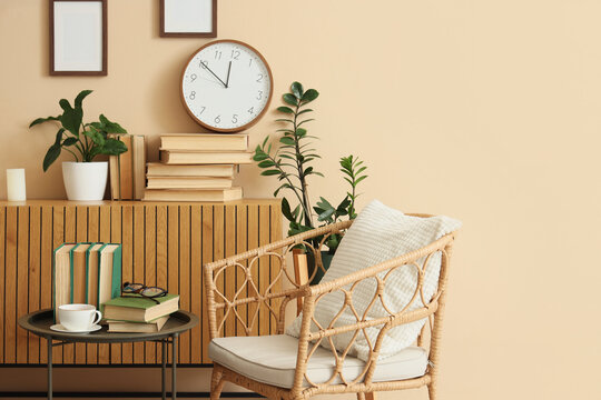 Cozy living room interior with a wicker chair, books, plants, and a wall clock on a beige background