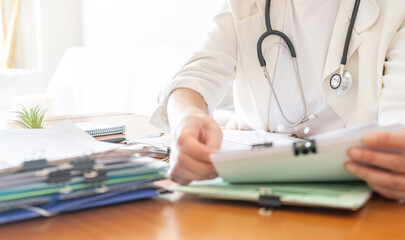 Fototapeta premium Healthcare professional wearing a white coat and stethoscope, working at a desk, reviewing important medical files and patient records in a clinic or hospital office
