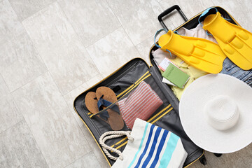 Open suitcase packed with summer vacation essentials including flippers, passport, and beach hat on a light tiled floor © Pixel-Shot