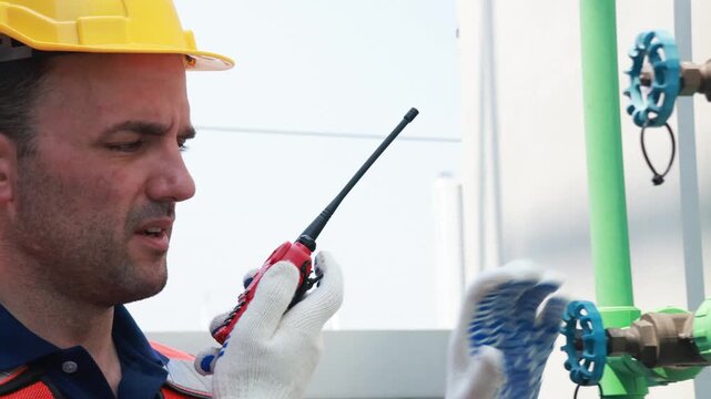 Male technician inspects the coolant inlet and outlet pipes of the cooling tower checks the flange connections and reports walkie talkie engine room while testing the cooling system.