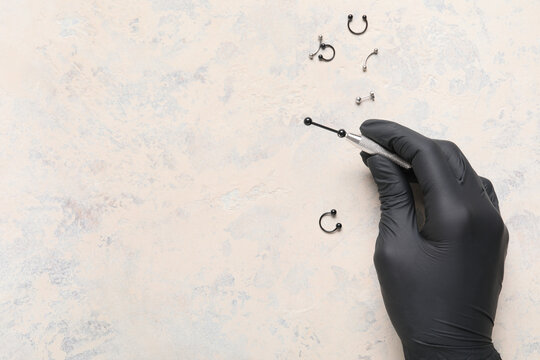 Hand in black glove holding a piercing tool with Various body jewelry on a textured background