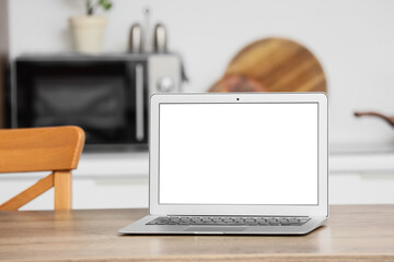 Fototapeta premium Laptop with blank white screen on a wooden kitchen table, home office and remote work