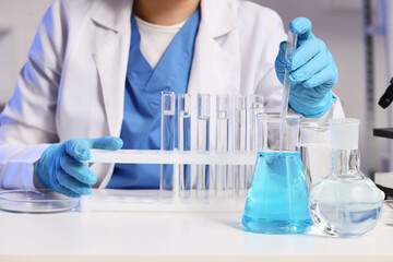 Fototapeta premium Female scientist taking water sample from flask on stand to test tubes at table in laboratory, closeup